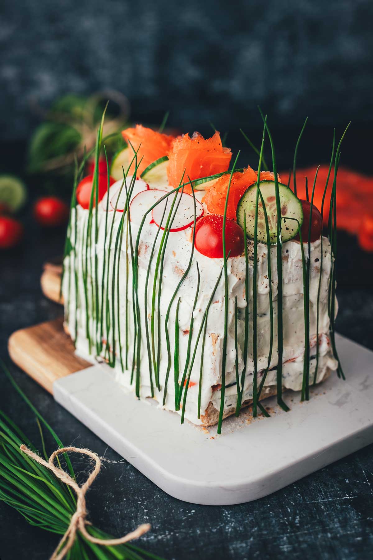 Seitliche Nahaufnahme einer mit Frischkäse bestrichenen Sandwichtorte, die mit frischem Gemüse, Lachs und Schnittlauchhalmen dekoriert ist.