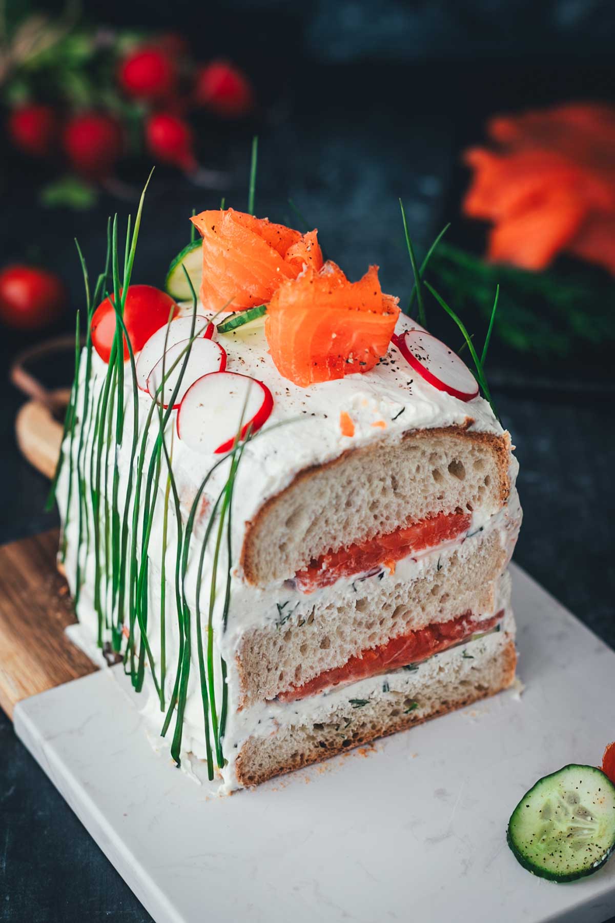 Seitliche Aufnahme, leicht schräg von oben einer Brottorte, die aus einem Kastenweißbrot mit Räucherlachs und Frischkäsecreme besteht.