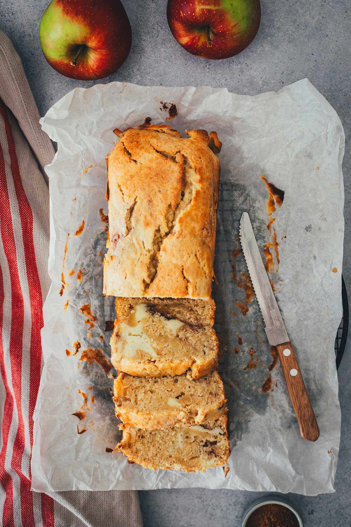 Topshot eines in Scheiben geschnittenen Apfelkuchens aus der Kastenform auf Backpapier mit einem Brotmesser daneben | moeyskitchen.com