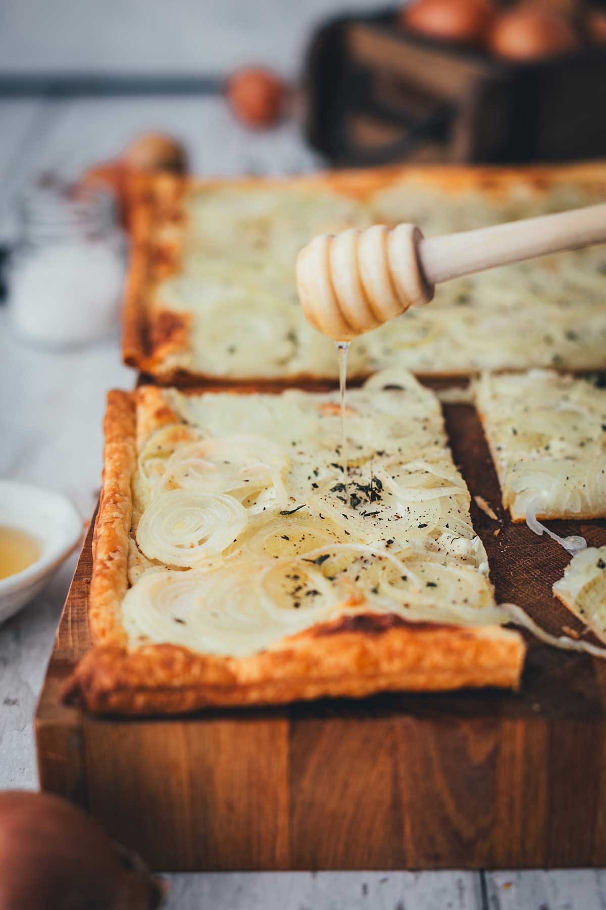 Stück Zwiebeltarte auf Holzbrett, mit Honig beträufelt und frischem Thymian bestreut | moeyskitchen.com