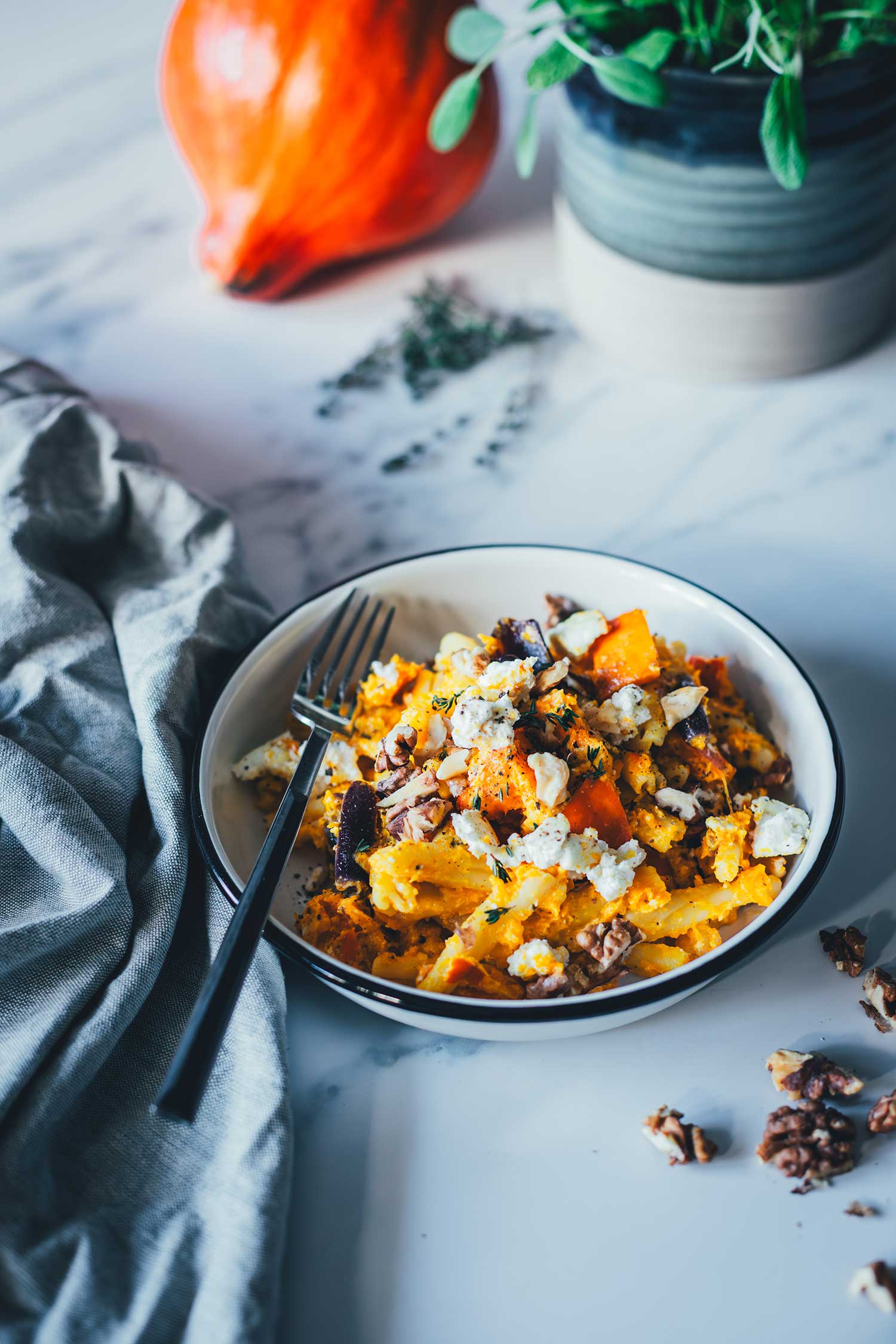 Kürbis-Feta-Pasta auf einem Teller serviert und mit Walnüssen bestreut. Im Hintergrund sieht man Kürbis und Salbei, im Vordergrund ein Geschirrtuch und Walnusskerne | moeyskitchen.com