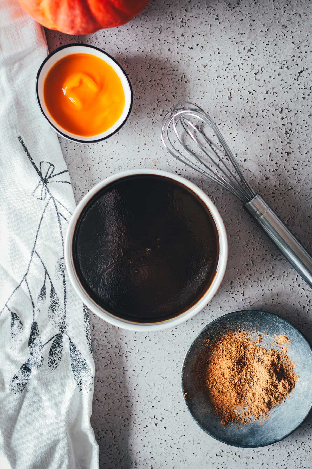 Topshot von einer kleinen weißen Schüssel mit Pumpkin Spice Sirup. Der ist karamellig und richtig dunkelbraun. Davor sieht man die Pumpkin Spice Gewürze und Zimt, dahinter sieht man Kürbispüree in einer kleinen Schüssel | moeyskitchen.com