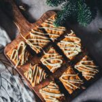 Weihnachts-Blondies mit weißer Schokolade, Cranberries und Pistazien auf einem Holzbrett, von oben fotografiert.
