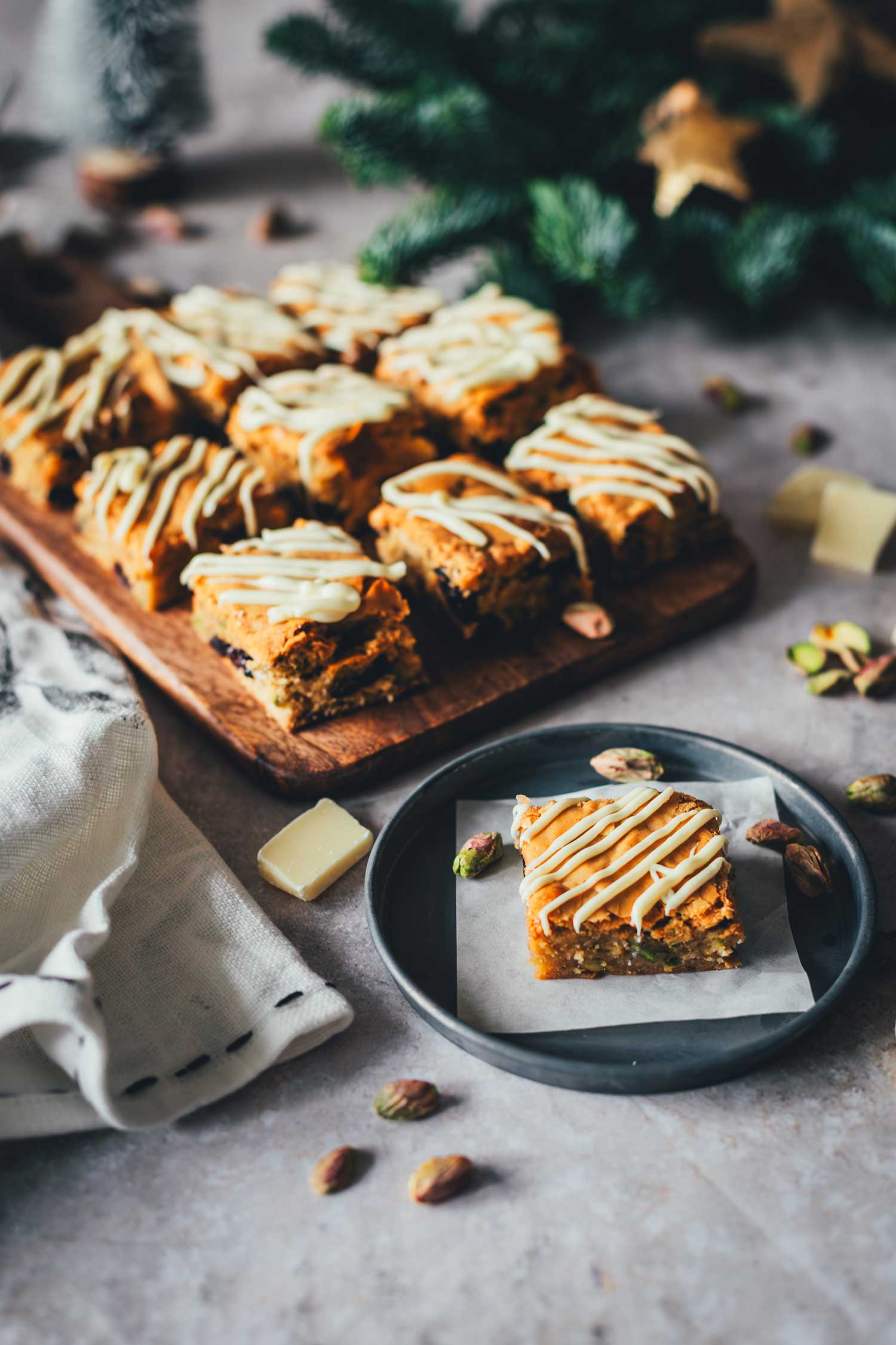 Weihnachts-Blondies im weihnachtlichen Setting mit Tannenzweigen und Deko im Hintergrund.
