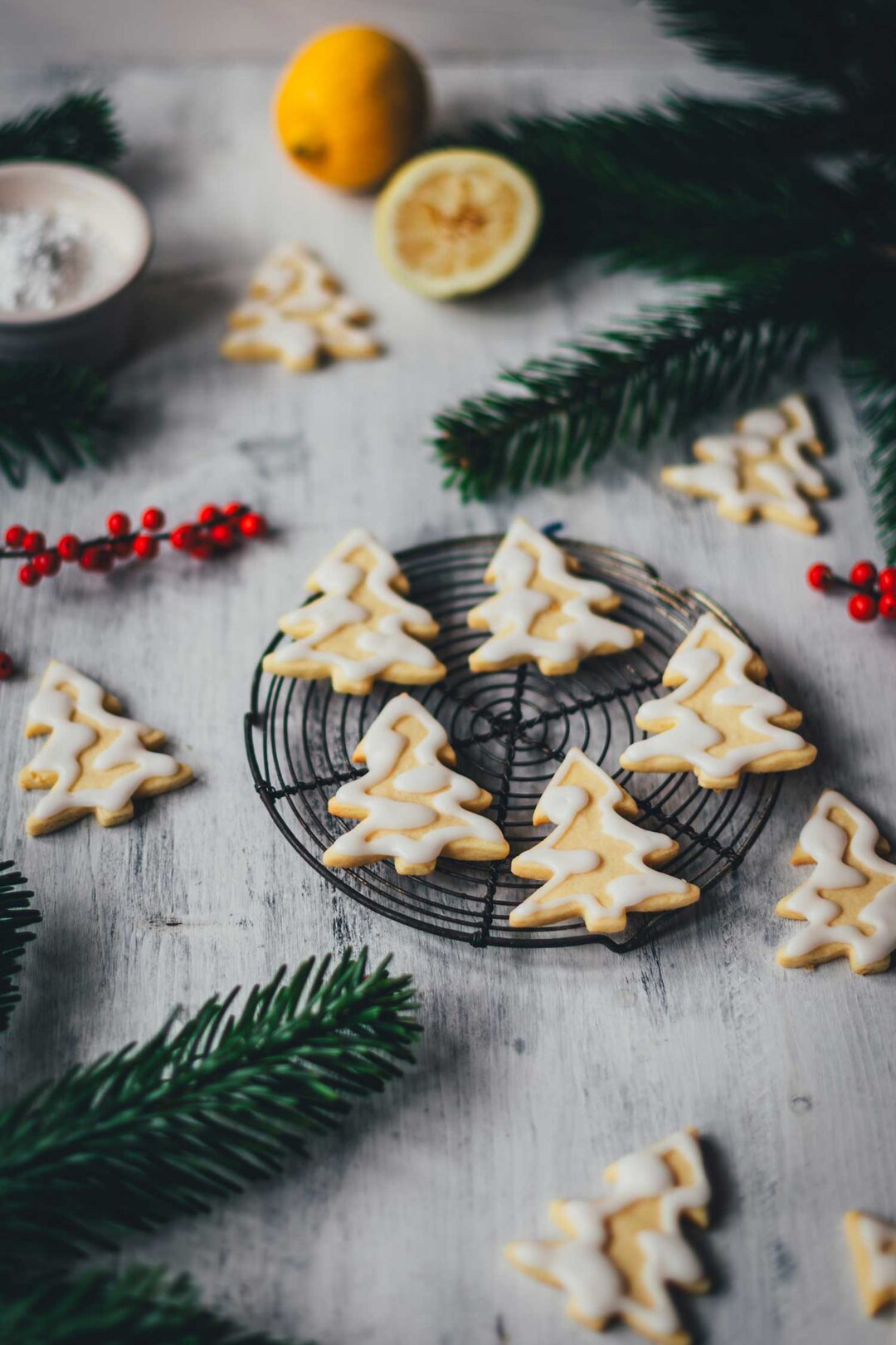 Seitliche Ansicht von Zitronenplätzchen mit Zuckergus inn Form von Tannenbäumchen auf einem kleinen Kuchengitter mit weihnachtlicher Dekoration drumherum | moeyskitchen.com