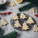 Seitliche Ansicht von Zitronenplätzchen mit Zuckergus inn Form von Tannenbäumchen auf einem kleinen Kuchengitter mit weihnachtlicher Dekoration drumherum | moeyskitchen.com