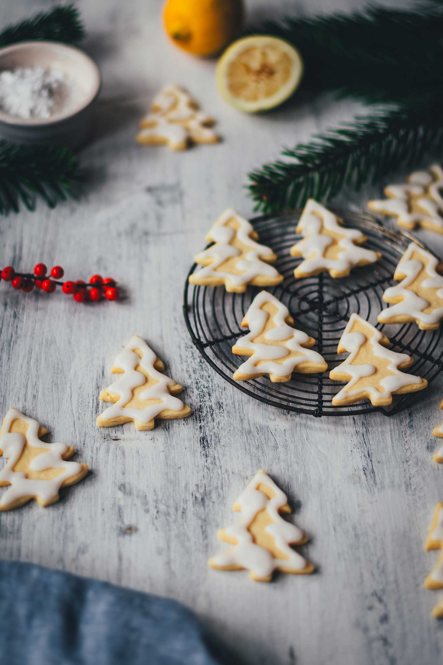 Seitliche Ansicht von Zitronenplätzchen mit Zuckergus inn Form von Tannenbäumchen auf einem kleinen Kuchengitter mit weihnachtlicher Dekoration drumherum | moeyskitchen.com