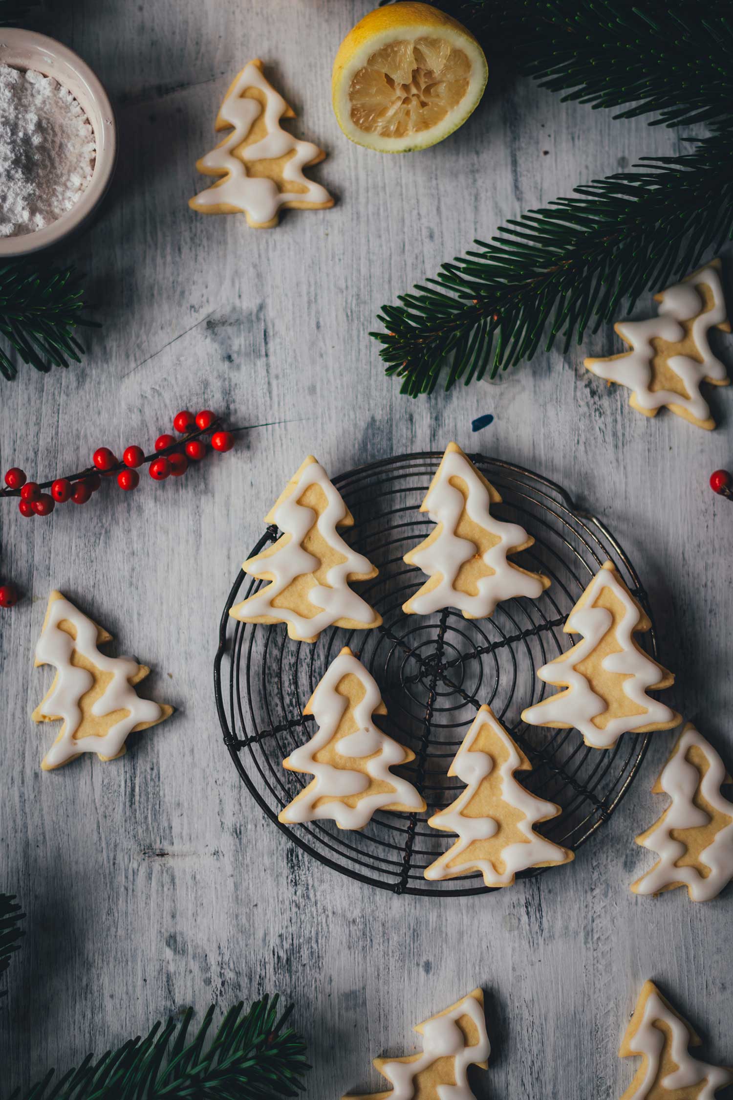 Topshotaufnahme von Plätzchen mit Zuckergus inn Form von Tannenbäumchen auf einem kleinen Kuchengitter mit weihnachtlicher Dekoration drumherum | moeyskitchen.com