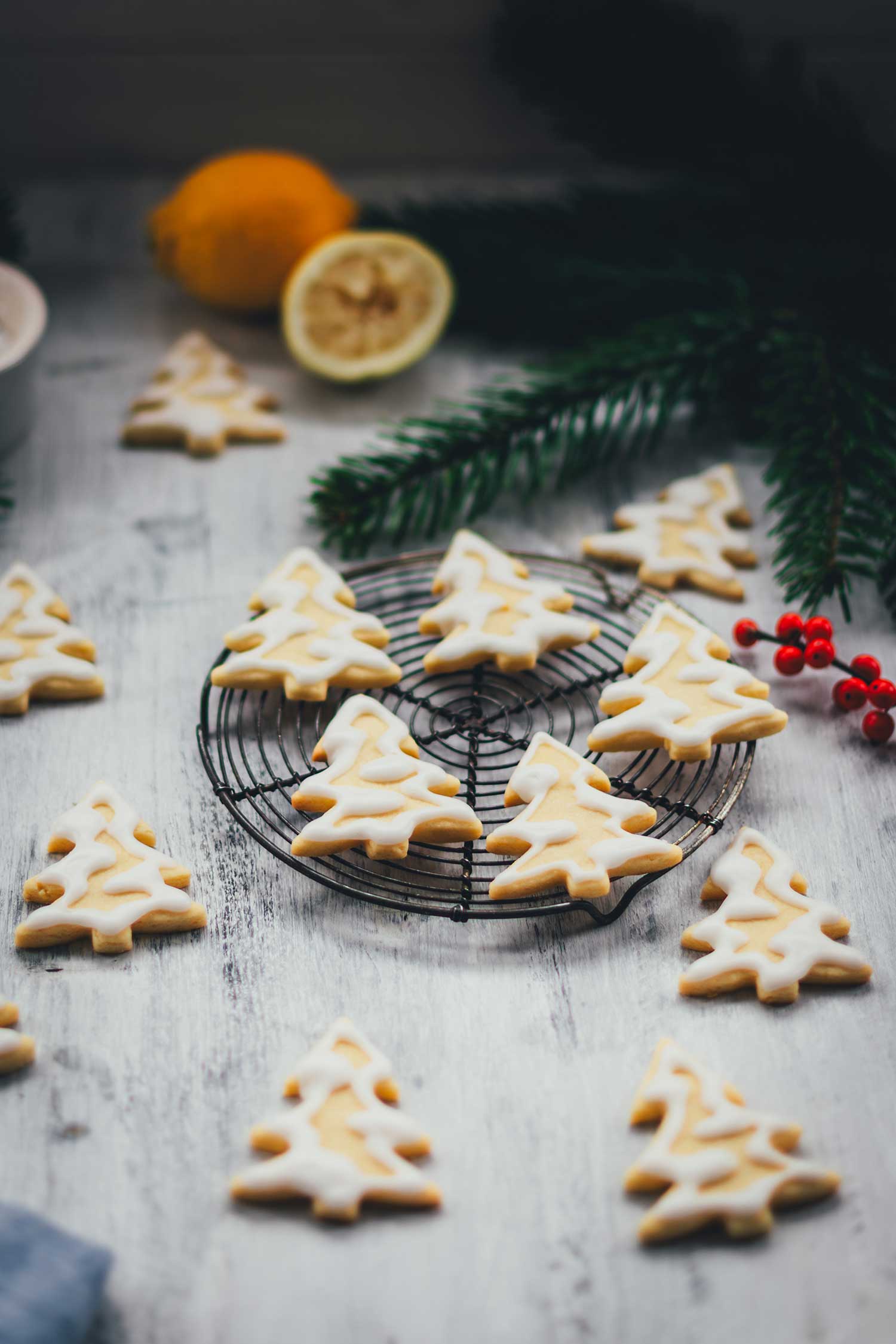 Seitliche Ansicht von Zitronenplätzchen mit Zuckergus inn Form von Tannenbäumchen auf einem kleinen Kuchengitter mit weihnachtlicher Dekoration drumherum | moeyskitchen.com