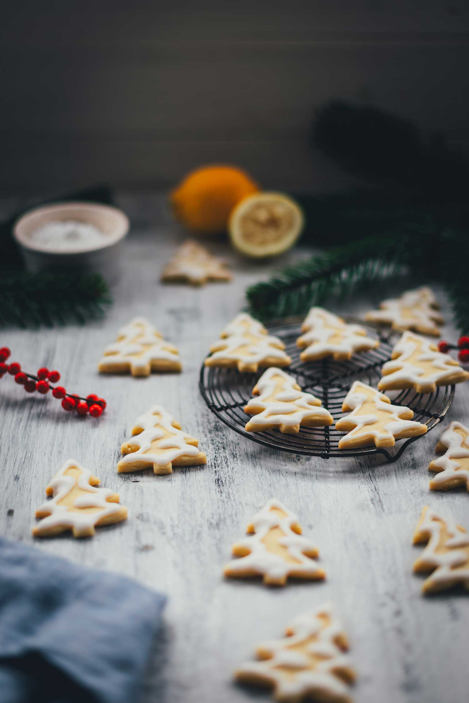 Seitliche Ansicht von Zitronenplätzchen mit Zuckergus inn Form von Tannenbäumchen auf einem kleinen Kuchengitter mit weihnachtlicher Dekoration drumherum | moeyskitchen.com