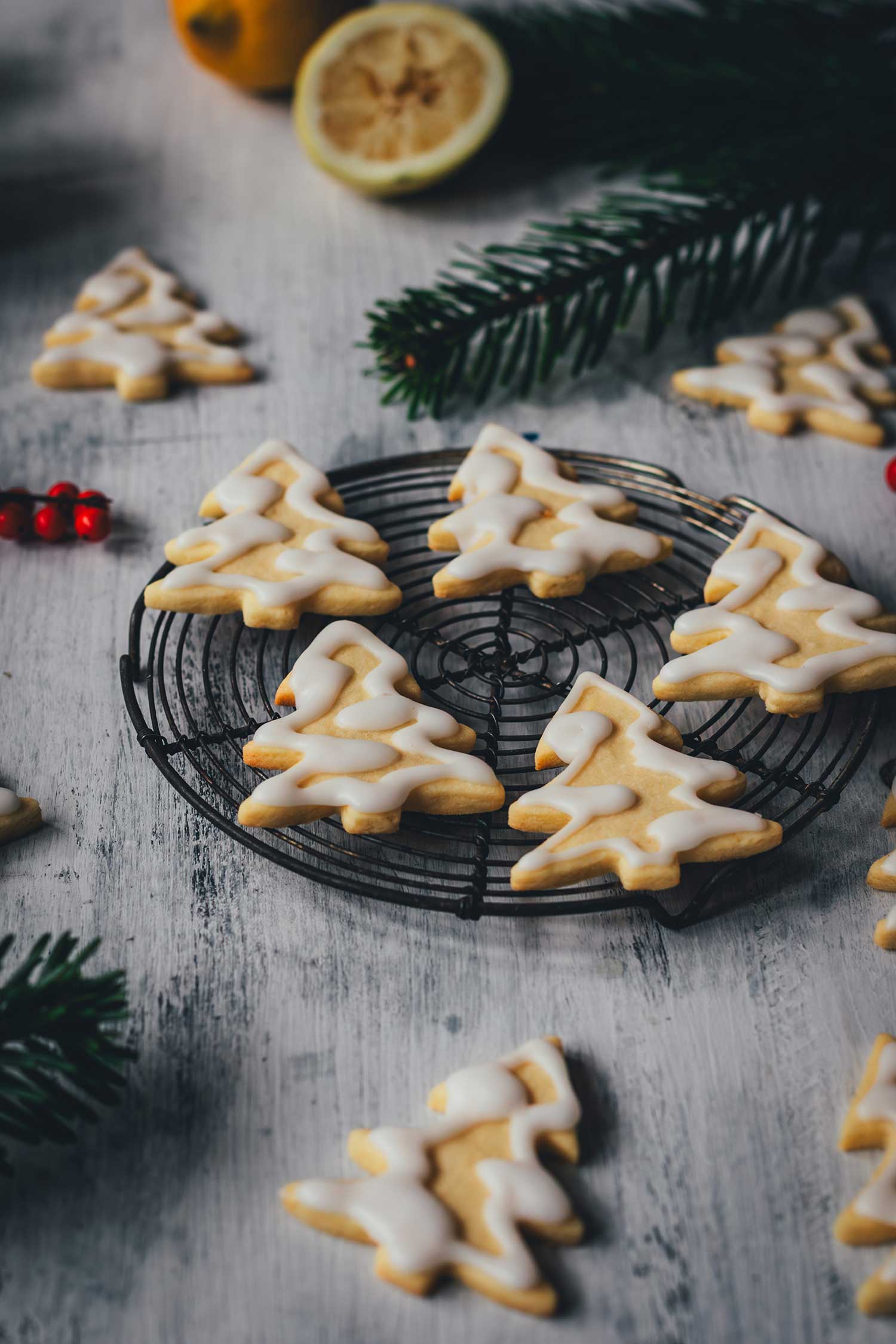 Seitliche Ansicht von Zitronenplätzchen mit Zuckergus inn Form von Tannenbäumchen auf einem kleinen Kuchengitter mit weihnachtlicher Dekoration drumherum | moeyskitchen.com