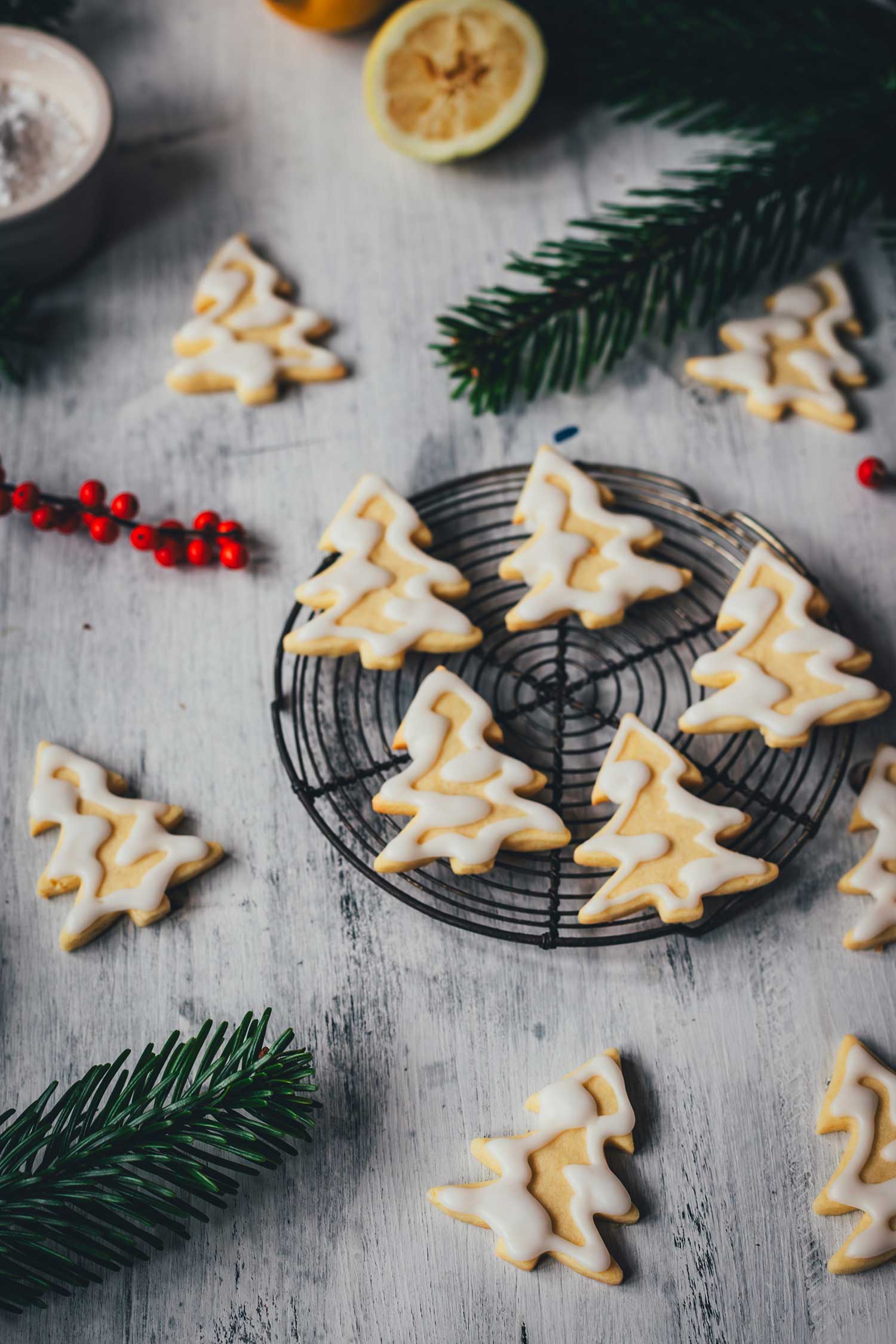 Seitliche Ansicht von Zitronenplätzchen mit Zuckergus inn Form von Tannenbäumchen auf einem kleinen Kuchengitter mit weihnachtlicher Dekoration drumherum | moeyskitchen.com