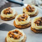 seitliche Ansicht von Apple Pie Cookies mit Mascarpone-Frosting und Apfeltopping auf einer Tortenplatte mit weißem Backpapier