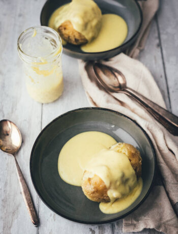 Zwei fluffige, goldbraun ausgebackene Dampfnudeln in dunklen Schalen, großzügig übergossen mit einer cremigen, hellgelben Vanillesauce – eines meiner liebsten Rezepte für den Februar.