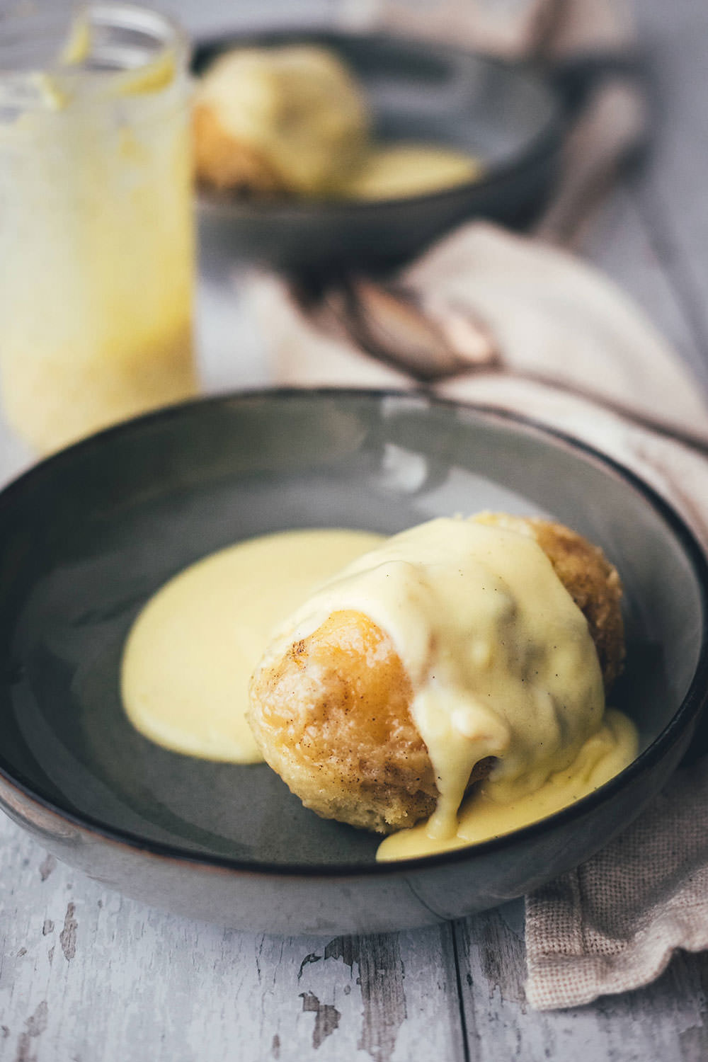 luffige, warme Dampfnudel mit einer dicken Schicht selbstgemachter, goldgelber Vanillesauce in einer tiefen dunklen Schale.