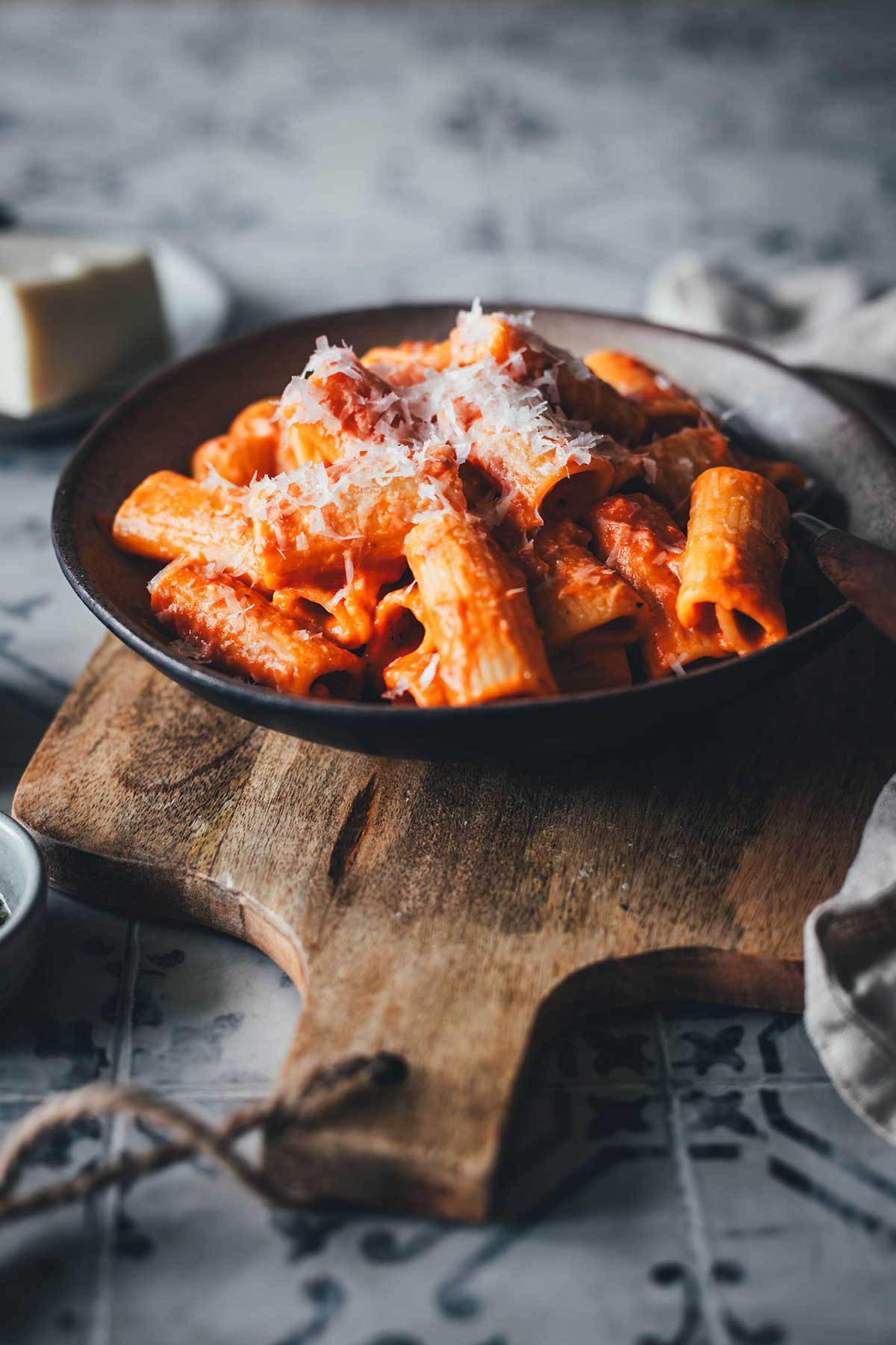 Pasta alla Vodka mit Rigatoni in einer leuchtend orangefarbenen Tomaten-Sahne-Sauce, getoppt mit fein geriebenem Pecorino auf einem rustikalen Holzbrett.