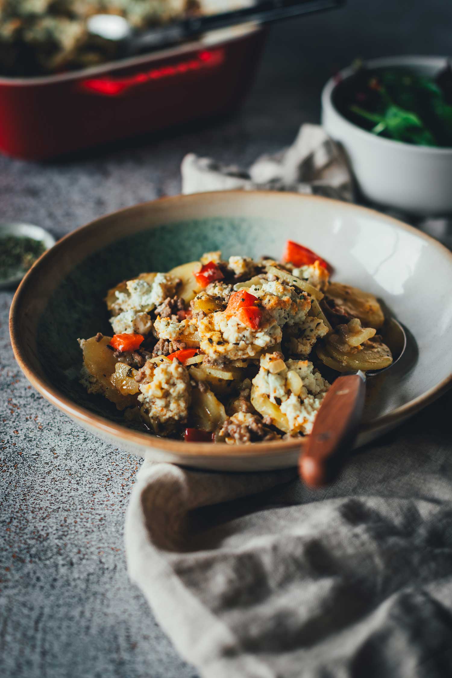 Servierfertiger Kartoffel-Hack-Auflauf mit Feta-Topping in einer Schale, im Anschnitt sieht man die cremige Sauce und das würzige Hackfleisch.