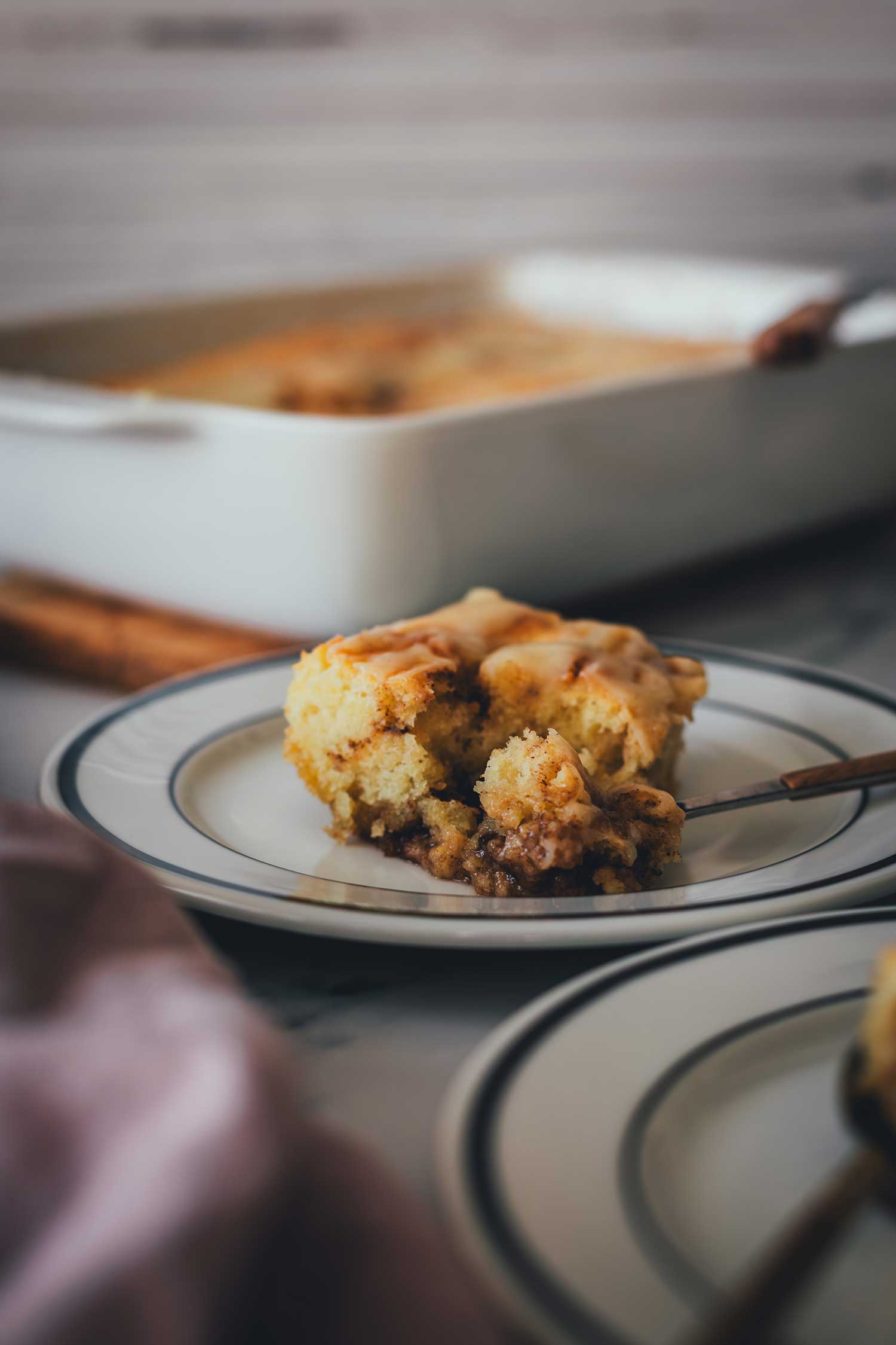 Frontale Nahaufnahme eines Stücks vom Zimtschnecken-Kuchen ohne Hefe. Man sieht die saftige Textur. Im Hintergrund steht die Auflaufform.