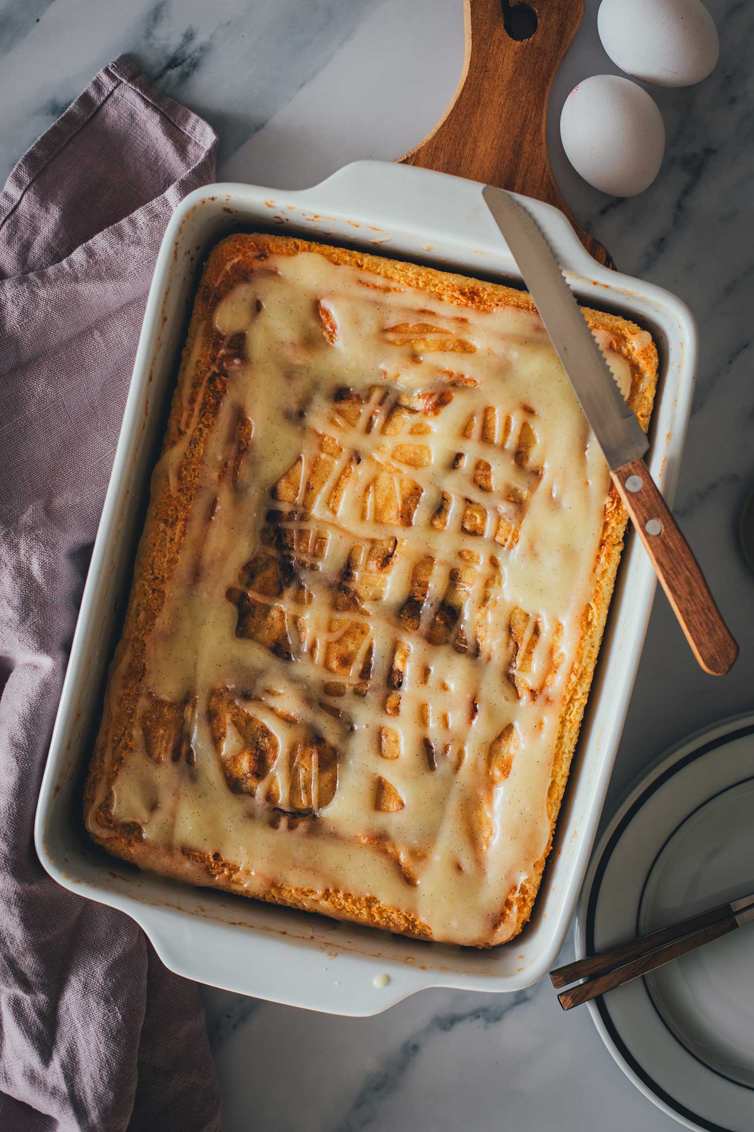 Topshot-Aufnahme des Zimtschnecken-Kuchens ohne Hefe vom fertig gebackenen Kuchen in der Backform, bestrichen mit Frischkäse-Glasur.