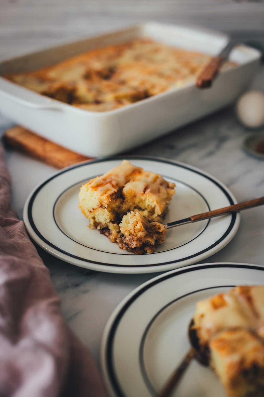 Zimtschnecken-Kuchen-ohne Hefe, serviert als Kuchenstücke auf Tellern. Man sieht, wie saftig und fluffig der Teig ist. Im Hintergrund steht die Backform.