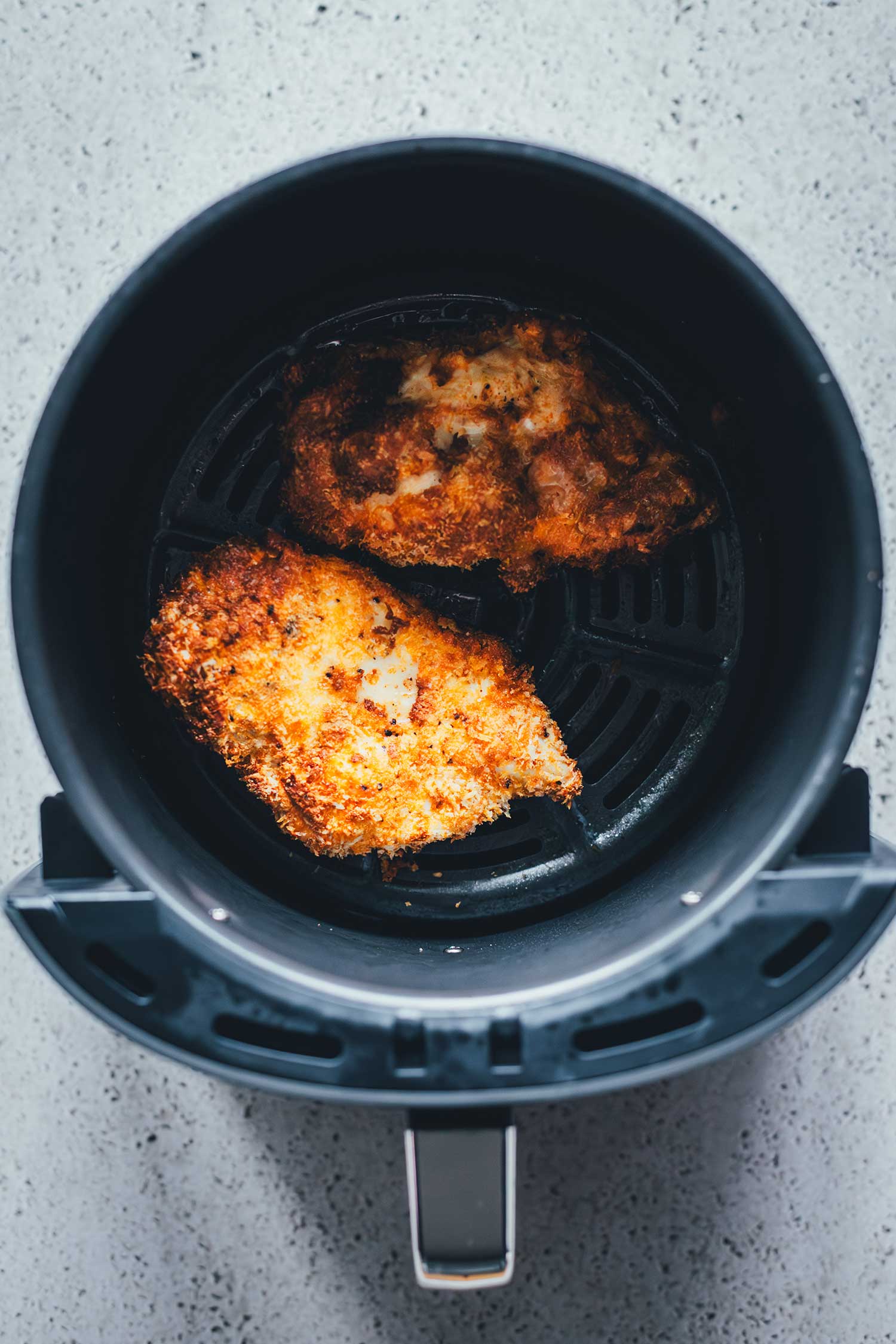 Zwei goldbraun und knusprig fertig gegarte Hähnchenbrustfilets mit Panko-Panade im Frittierkorb des Airfryers nach 15 Minuten bei 200 Grad