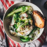 Grüner Spargelsalat mit Burrata, Pistazien und Rucola in einer hellen Schale, daneben getoastetes Sauerteigbrot