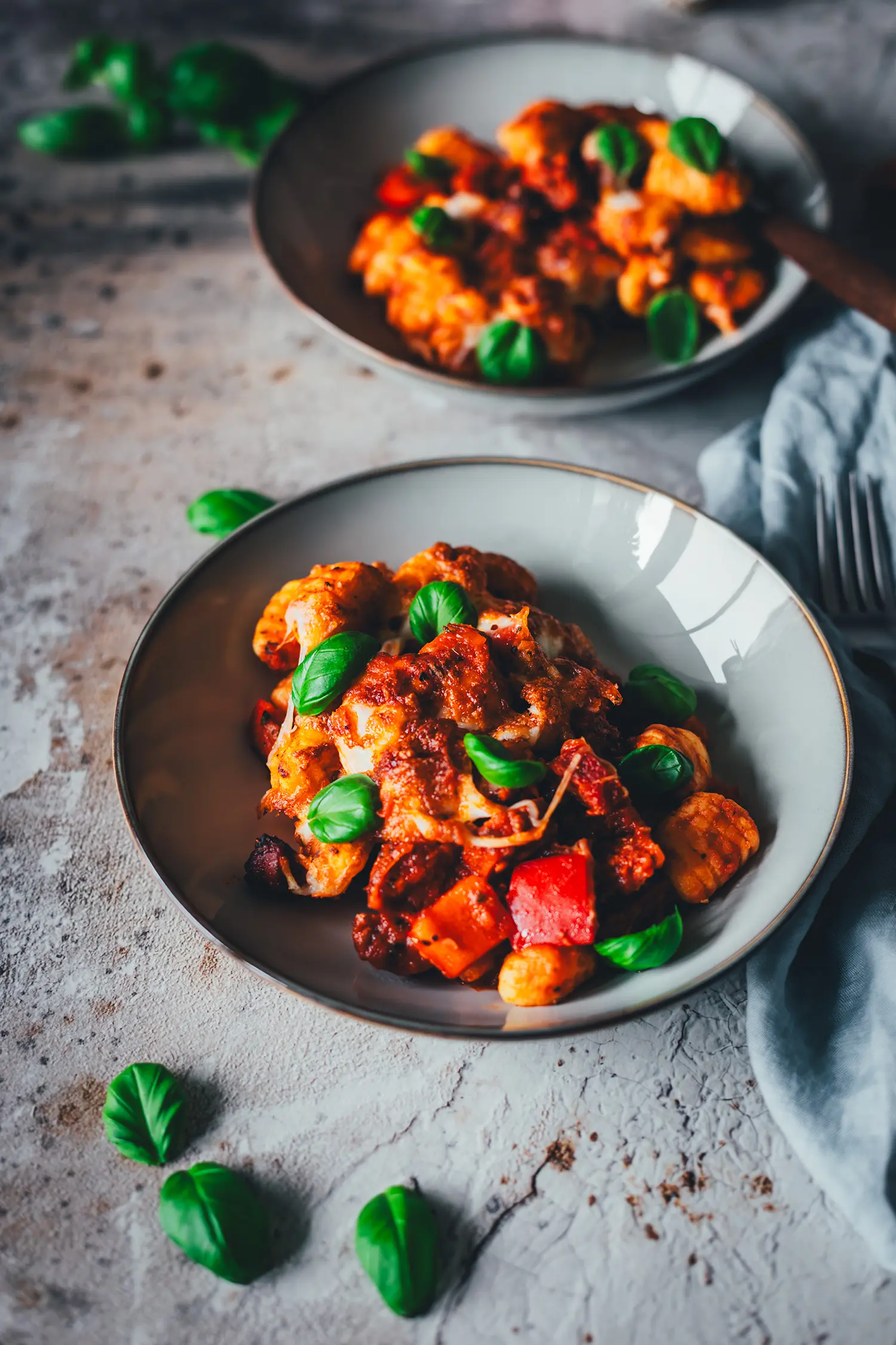 Zwei angerichtete Portionen Gnocchi-Auflauf aus dem Airfryer mit Chorizo, Paprika und Basilikum auf hellem Untergrund